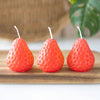 Three strawberry-shaped orange candles displayed on a wooden surface.