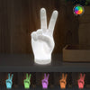 Hand-shaped lamp displaying a peace sign with color-changing capabilities on a wooden background.