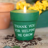 Green candle in a pot with 'Thank you for helping me grow' text, surrounded by soil and plants.