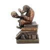 Bronze statue of a monkey with a skull on a stack of books against a white background