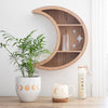 A wooden crescent moon wall shelf with cut out sparkle designs, displayed on a wall above a shelf with a plant and other decorative items.