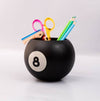Black billiard ball-shaped holder with stationery items on a light gray background