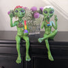 Two green alien figurines on a black surface with a neutral background