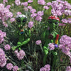 Two green alien figurines sitting outdoors among pink flowers