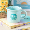 A blue ceramic mug with a smiling face design and the text 'you are so loved' 