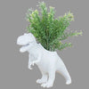 White dinosaur-shaped planter with a plant against a brick wall background